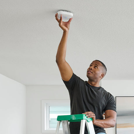 man on ladder installing smoke alarm on ceiling 