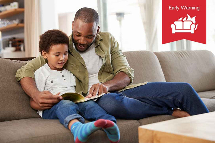 Father reading to his son on the couch with an overlaid early warning icon